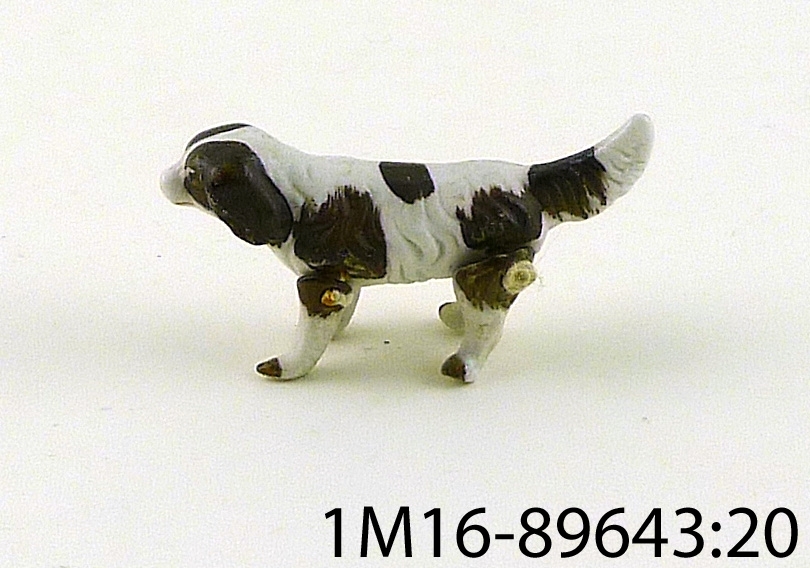 Figurin, hund av porslin, brun och vit, ligger ner eller står upp beroende på hur en placerar benen.