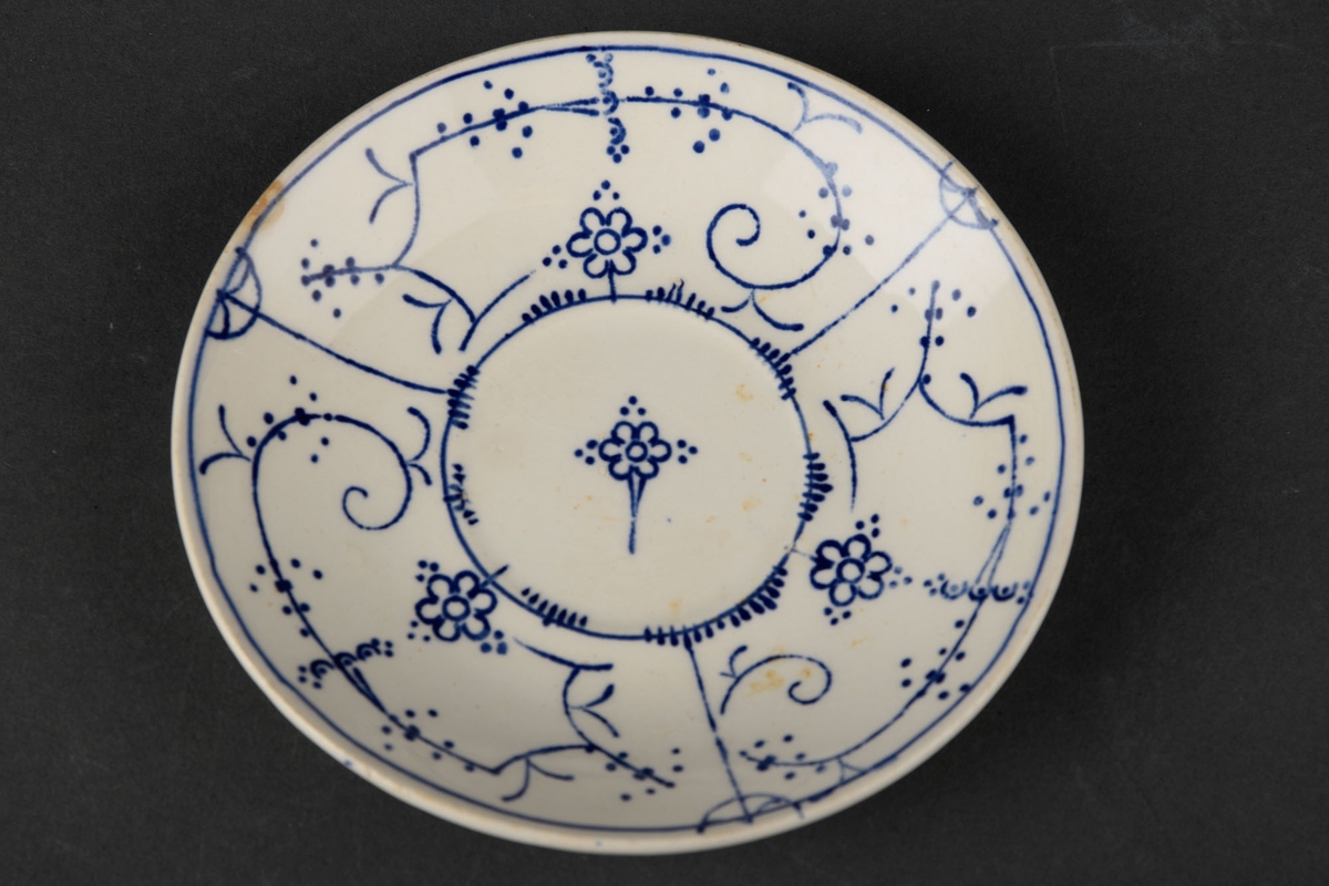 1 hvit tallerken med blå håndmalt dekor av bl.a. blomster.