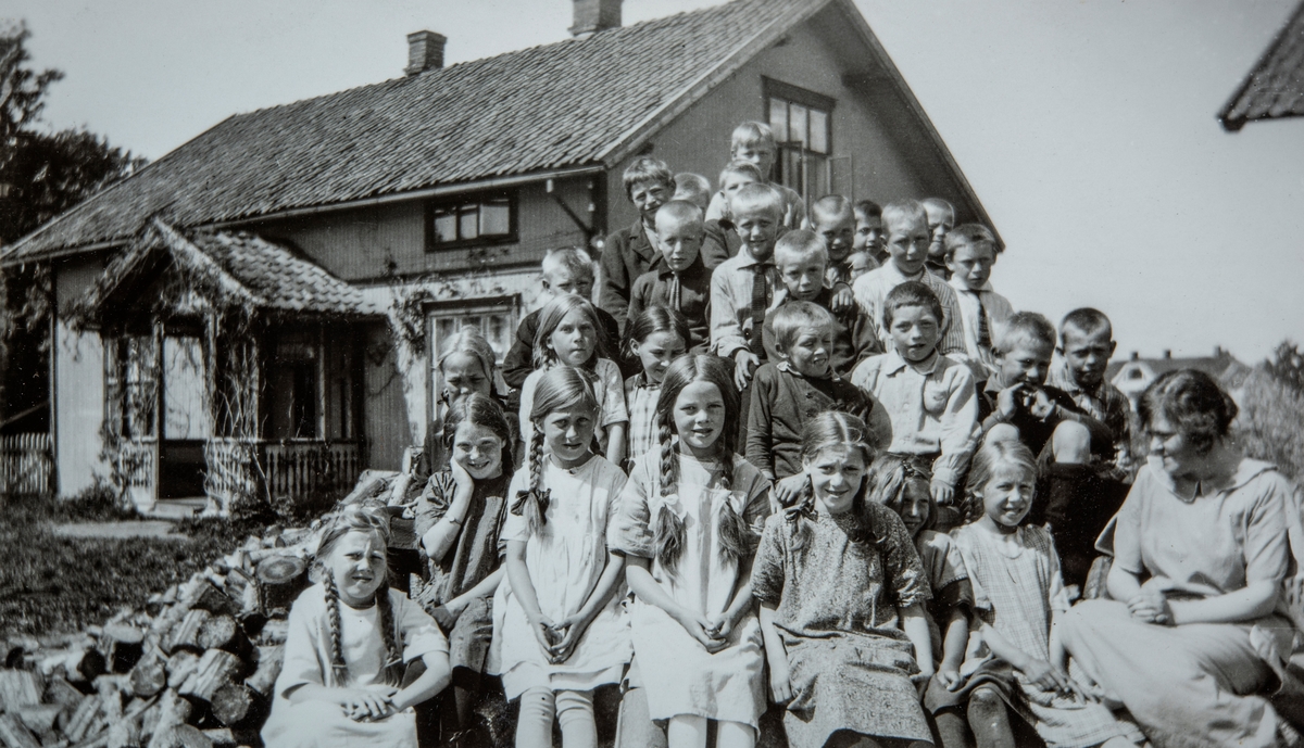Skoleklasse foran Klokkergården i Vang.  Kjøs (81/1). Ole Andersen Kjøs eide Stanger i Vang fram til 1931. Sønnen Anders gikk de første åra på Kirkekretsen skole (senere Ridabu skole) i Vang. Her er elever fra skole sittende i vedhaugen foran Klokkergården (9/1).