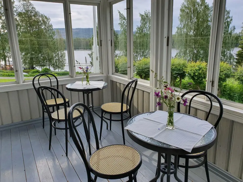 En glassveranda med to bord med blomster og stoler plassert rundt bordene.