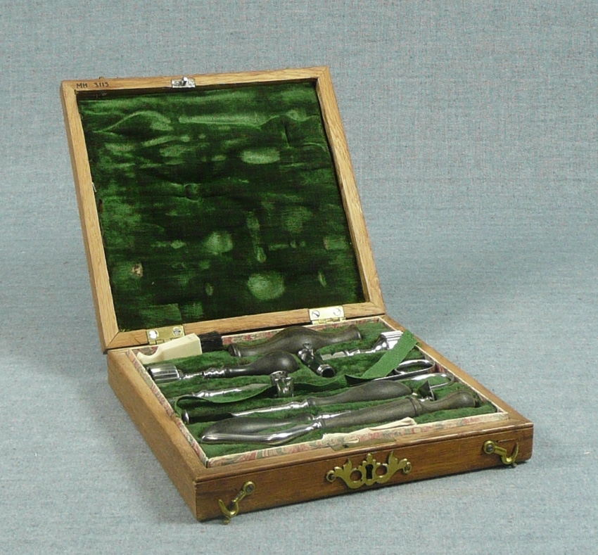 Etui av trä med grön inredning. Innehåller: 8 instrument med svarvade trähandtag, 2 handtag, 1 borste av elfenben. Handskriven text (liknar någon form av recept).
