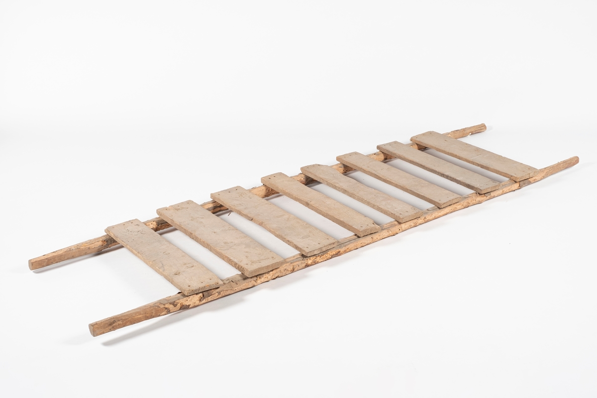 Rektangulær båre, brukt til å bære slaktegris. Består av 8 planker lagt på tvers og spikret fast til to trestenger. Det er rester av bark på stengene, og endene som er håndtak er spikket til for bedre grep.