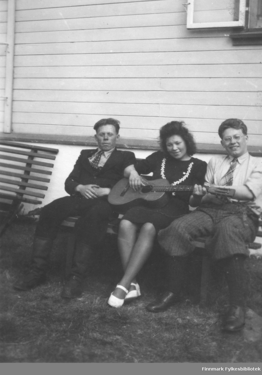 Tre pentkledte personer sitter på en benk. Til venstre på bildet sitter Mathis Mathisen og Samuel Mathisen. Sted og kvinnen i midten er ukjent.