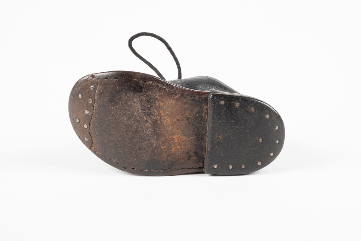 Et randsydd barnesko (høyre sko) av lær. Skoen har snøring med runde lisser. Maljene er av metall. Sålen er av lær og er forsterket med spiker på hælen og ved tuppen på undersiden.