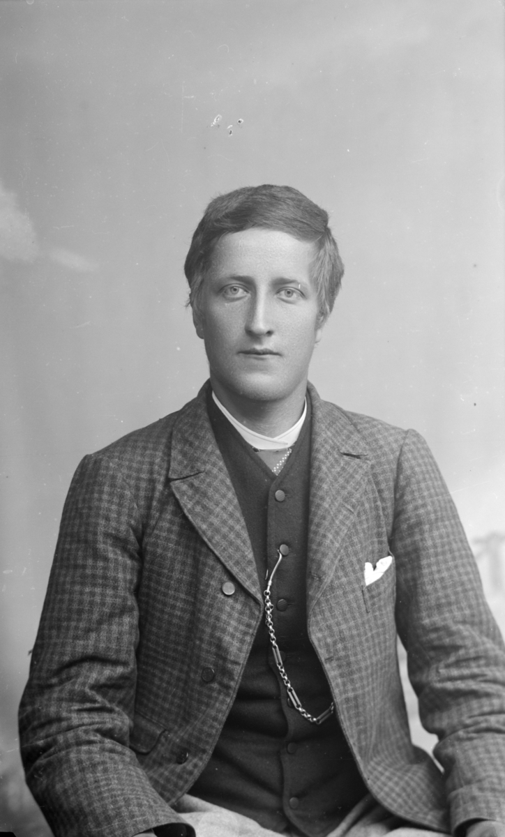 Portrett av yngre mann i rutet jakke og mørk vest