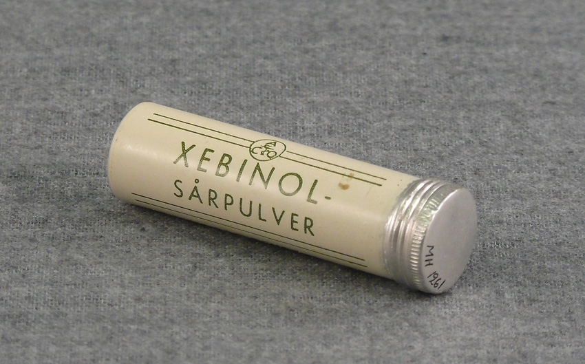 Tub i metall med skruvlock, delvis vitmålad, och med grön text: Xebinol - sårpulver. Apoteket Åtvidaberg.