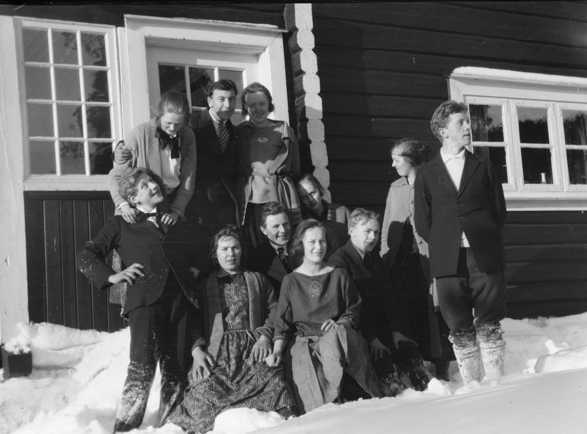Ungdommer i snøen utenfor en tømmerbygning.