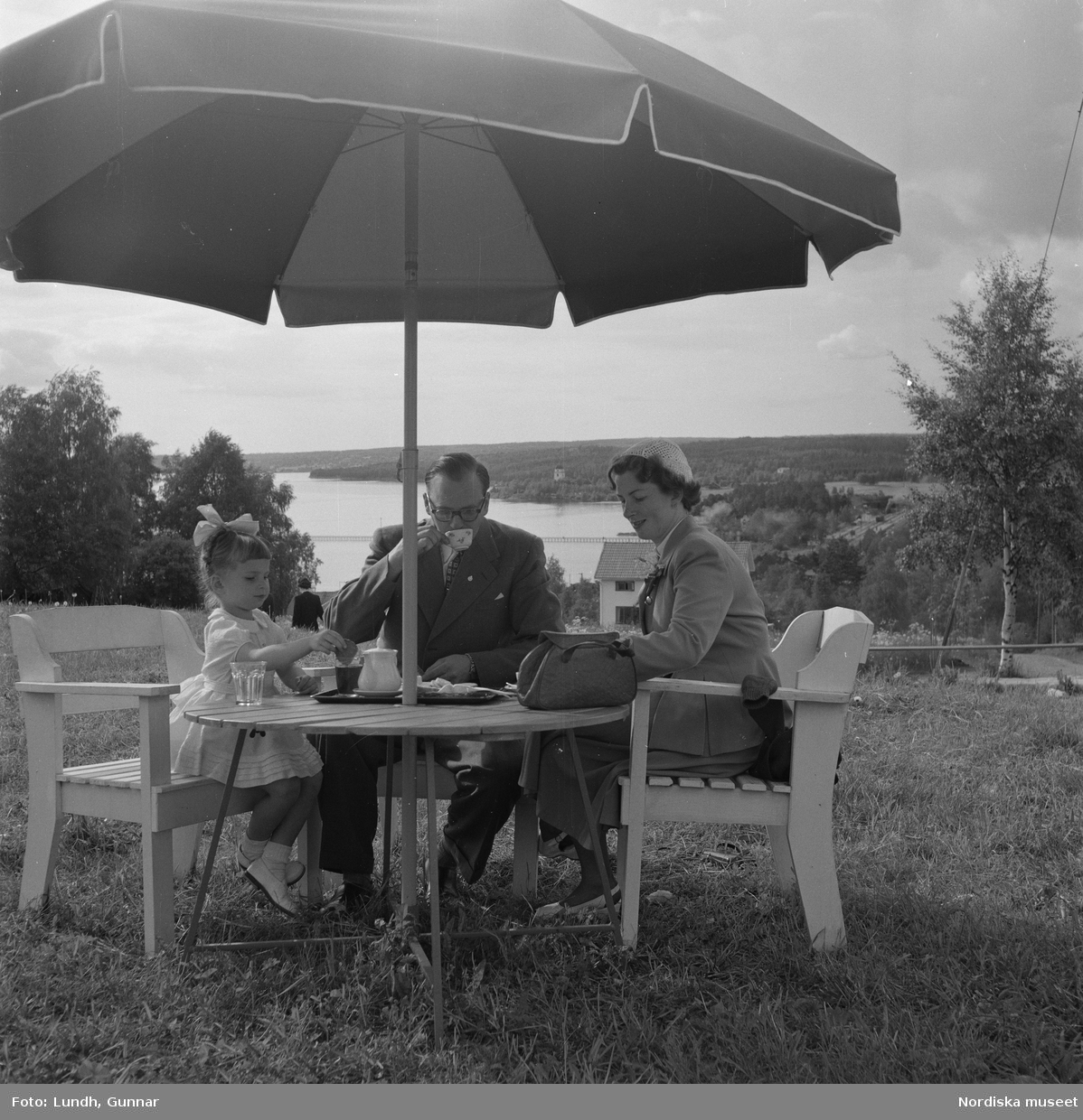 Motiv: (ingen anteckning) (Lerdalshöjden) ;
Tre män spelar fiol vid en midsommarstång, vuxna och barn dansar kring en midsommarstång, en pojke och en kvinna står på en balkong, en flicka - en man och en kvinna sitter vid ett trädgårdsbord under ett parasoll och äter, tomma flaskor av "Loranga" står på ett trädgårdsbord med en midsommarstång i bakgrunden.