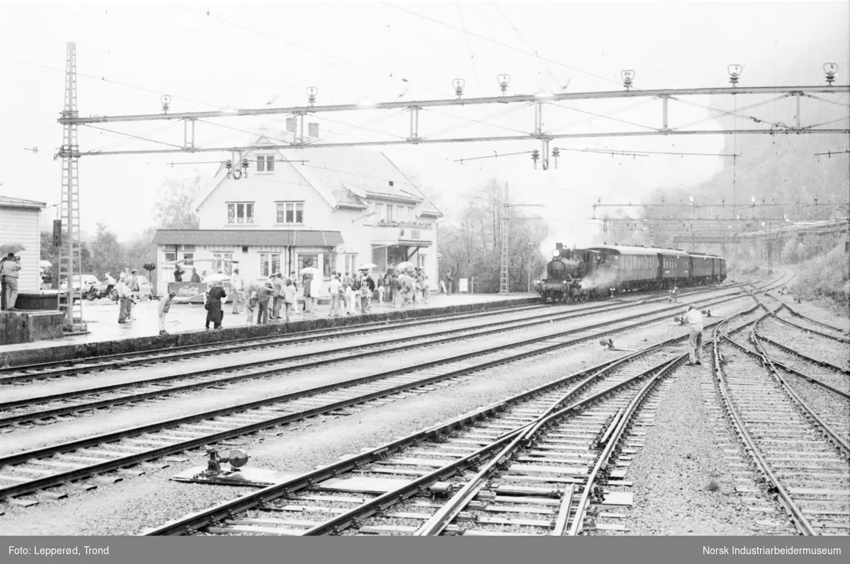 Togskinner, lokomotiv og mennesker på togstasjon.
