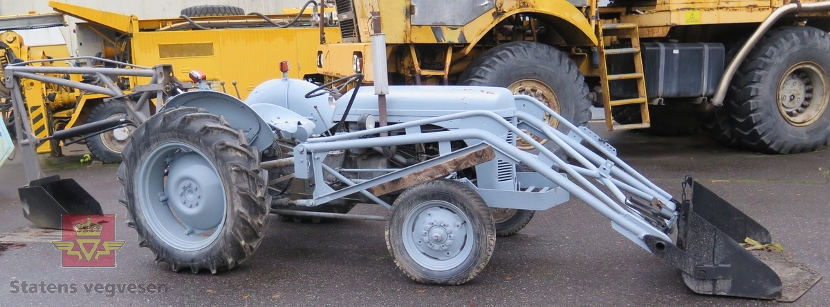Ferguson TEA20. Grå traktor med lasteapparat foran og graveaggregat bak. Motoren er en 4-sylindret bensinmotor fra Standard Motor Company.