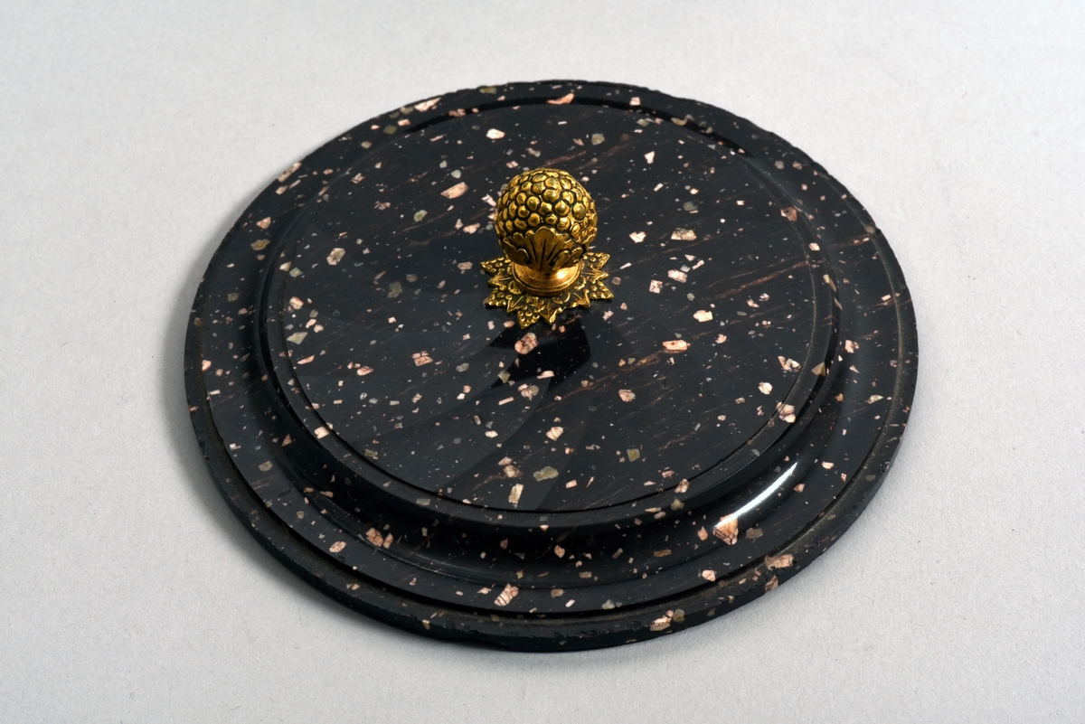 Dosa med lock av porfyr från Älvdalen. Fasettslipad dosa. Locket har en knopp i forma av en förgylld vindruvsklase av brons.