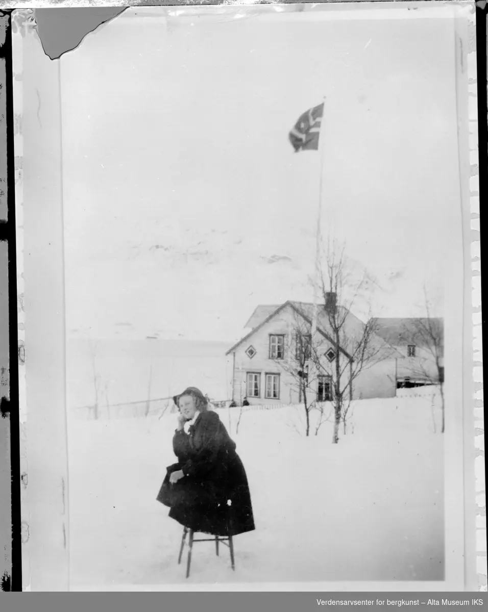 Vinter bilde av en kvinne som sitter på en stol utfor et hus med flagget heist.