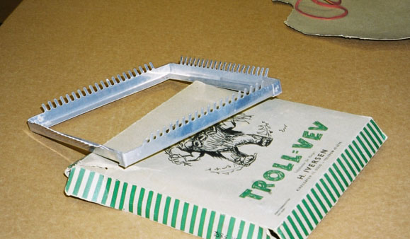 Metallramme med "tenner" i pappeske medfølgende bruksanvisning.