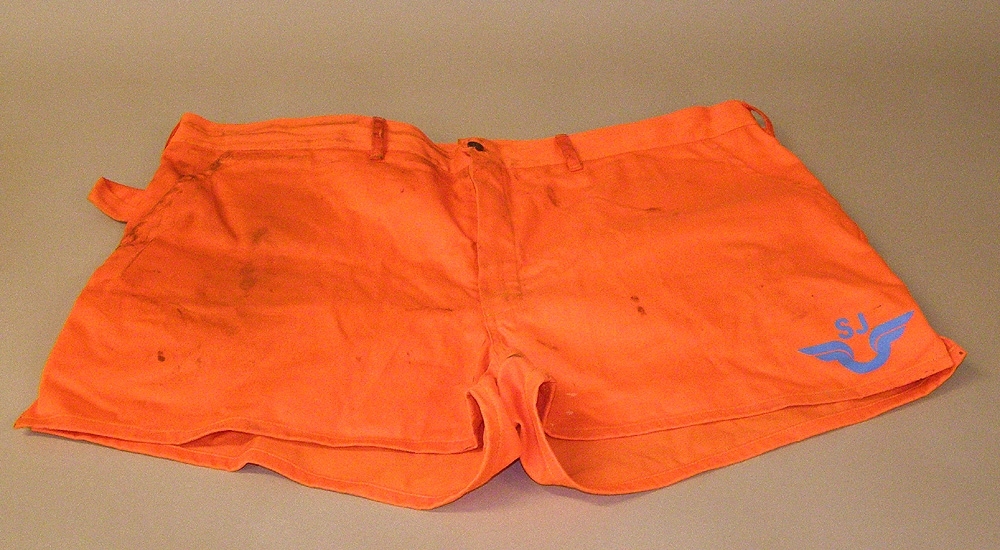Shorts eller kortbyxa av orange textil med SJ-logotyp i blått på vänster ben.

Storlek 62