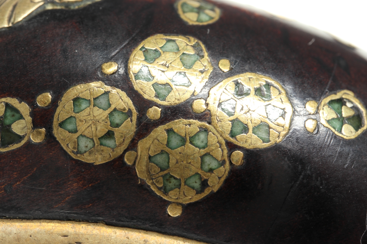 Slaglåspistol av 1600-talstyp med koniskt utsvängd pipmynning omändrad från flintlås under 1800-talet. Den är försedd med dekorerad helstock bestående av inläggningar i mässing och emalj i form av blomformade ornament. Kolvkappan av mässing har en heltäckande gravyr som avslutas med en ansiktsliknande kolvknapp. Runt kolvknappen löper en bokstavsfris som visar "NANNAN". Låset och pipan av stål har bladliknande gravyr. Sidoblecket består av en gjuten/graverad mässingsplåt. Tumplåten av mässing har ett växtornament, samt att varbygeln och avtryckaren är tillverkade av graverad mässing. I laddstocksrännans bakre del finns en dekorerad spetsrörka. Även det främre rörkoret i mässing har enklare utsmyckning. Det främre pipbeslaget är av ben. Pipan är slätborrad med en innerdiameter på 17 mm. 
Inskrivet i huvudkatalog 1974