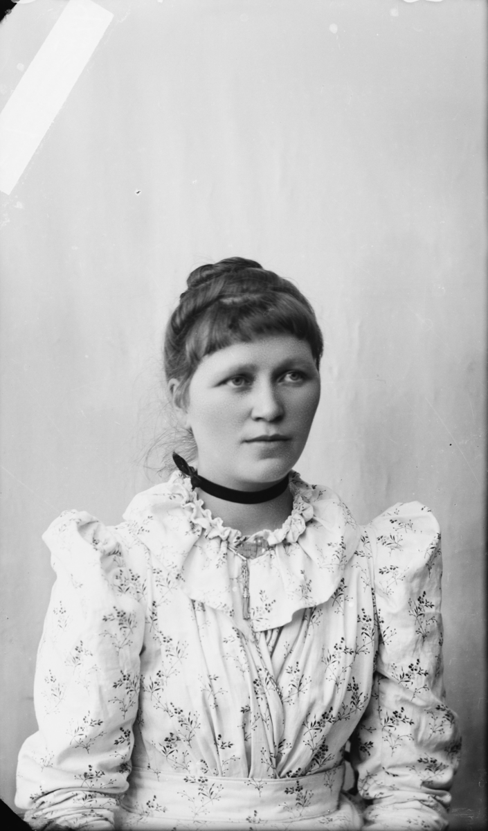 Portrett av yngre kvinne med oppsatt hår og lys kjole med puffermer. Etter MPLs regnskapsbok er dette Anna Kvam, Gaupen Meieri, Ringsaker