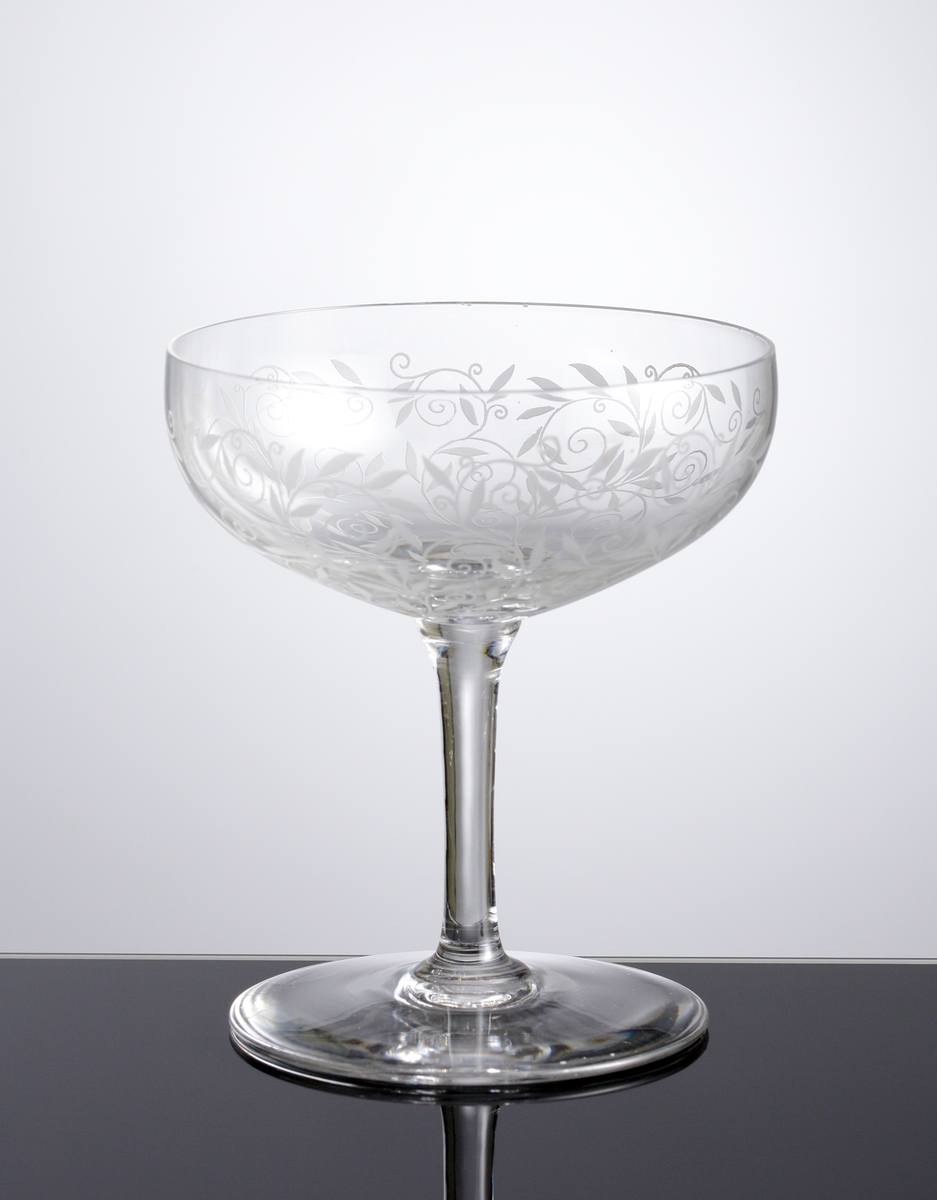 Champagnegkupa i ofärgat klarglas med dekor bestående av etsade bladrankor.