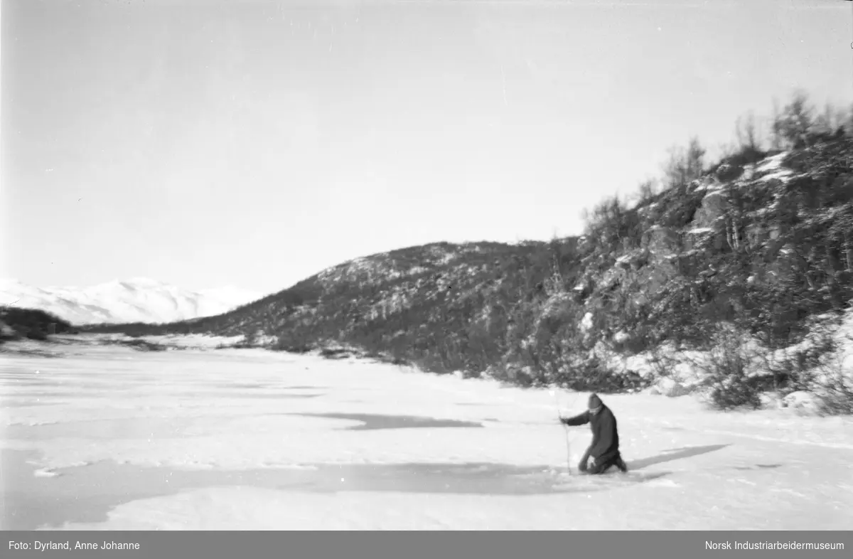 Jon Åkre sitter på isen med kvist i hånden på svartetjønn, Møsstrond