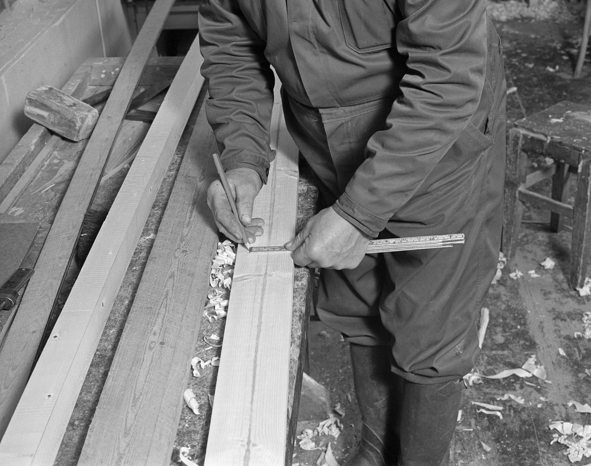 Bygging av fløterbåt i Glomma fellesfløtingsforenings verksted Breidablikk ved kommunesenteret Flisa i Åsnes i november 1984. Båttypen ble for øvrig kalt «Flisabåt», men denne modellen var egentlig utviklet av John Dybendal (1904-1985) omkring 1930. Målet var å kunne levere en robåt som passet i elva Flisa. Dybendal bygde sjøl slike båter fram til 1949. Glomma fellesfløtingsforening hadde vært en viktig kunde hos Dybendal, og da han gav seg som båtbygger ble virksomheten flyttet til denne virksomhetens verksted for Solør-regionen, hvor båtbygging ble vinteraktivitet for et par av karene som hadde vassdraget som arbeidsplass sommerstid. Det var maler til alle båtdeler, og skroget ble bygd på tverrmaler som ble festet til kjølen. Dette var hjelpemidler som gjorde det mulig for fløtere med reletivt liten handverkserfaring å bygge denne båttrypen og oppnå den standardiserte formen som fløterkameratene var vant med. De fleste flisabåtene fikk jernspanter, for det var krevende å finne de krokvokste emnene som gav de beste spantene. Ettersom Norsk Skogbruksmuseum dokumenterte båtbygginga ville karene likevel bruke trespanter på denne siste båten de bygde. Da dette fotografiet ble tatt merket Lars Bernhard Olastuen (1927-1998) opp hvordan han skulle sammenføye de to komponentene som skulle bli til en T-formet kjøl ved hjelp av tommestokk og blyant.

Båten som var under bygging da dette fotografiet ble tatt ble seinere overlatt til Norsk Skogbruksmuseum, der den fikk nummer SJF.07823 i gjenstandssamlinga. Den er 518 centimeter lang og 153 centimeter bred. Odd Jensen har seinere lagd oppmålingstegninger, som også finnes i museets arkiv.