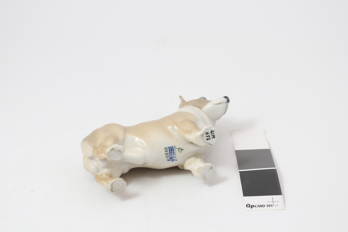Figur i porselen, formet som en mindre hund i brunt med hvit hals og underside. Produsentstempel på undersiden.