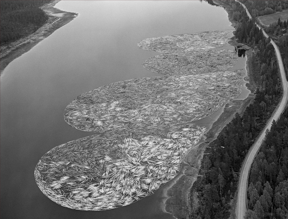 Fortøyde tømmerbommer ved land i Valmen, ei vik i den nordvestre enden av Osensjøen, der sjøen har avløp til elva Søndre Osa. Nordre Osen, Åmot kommune, Hedmark. Fotografiet er tatt fra fly.