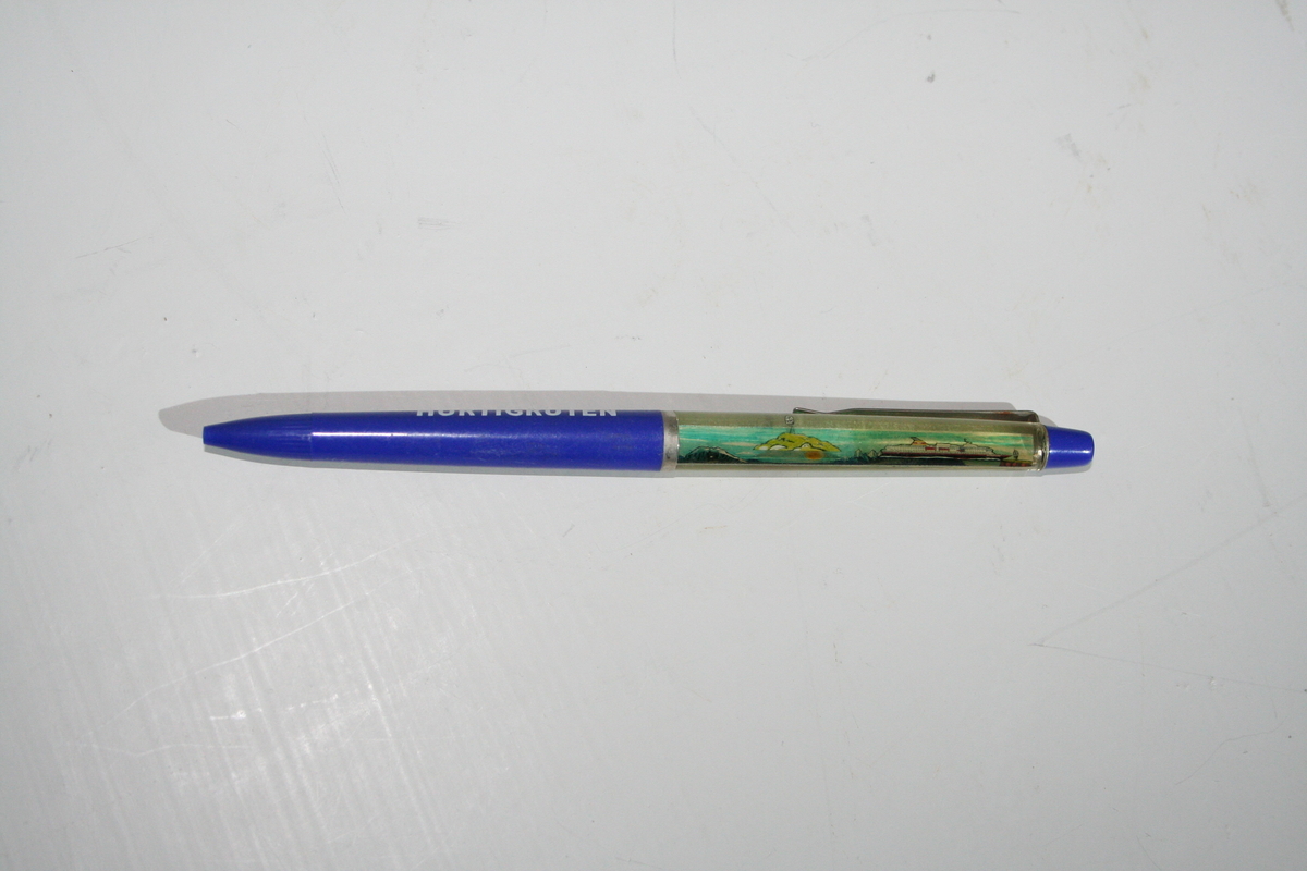 Plastikk kulepenn. Suvenir fra M/S "Nordkapp". Pennen har en "flytende " hurtigrute i skaftet som passerer Nordkapplatået. Rederiflagget til Ofotens dampskibsselskap er tegnet på.
