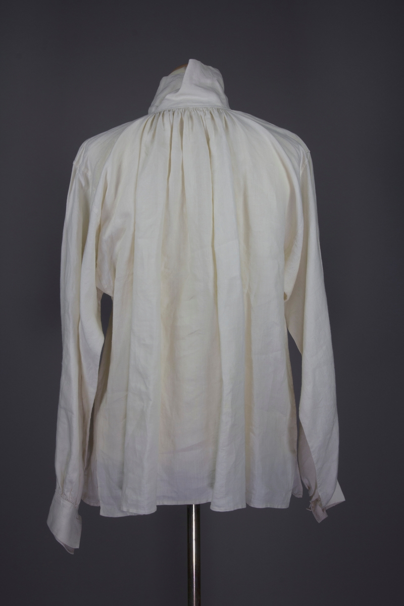 Skjorta av blakt tuskaftsvävt blekt linne. Stripade rynkor mot kragen och manchetterna på varje ärmslut. Krage och manchetter stängs med två hopsydda trådknappar. Till stora delar handsydd.