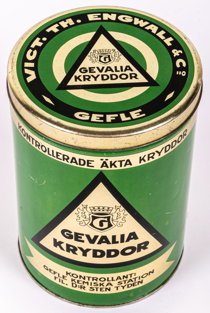 Kryddburk i litograferad plåt. Cylindrisk med trycklock. Grön med detaljer i guld och svart. Text: "GEVALIA KRYDDOR" och "VICT.TH. ENGWALL & Co GEFLE", "PRIMA MALEN KANEL" m.m.