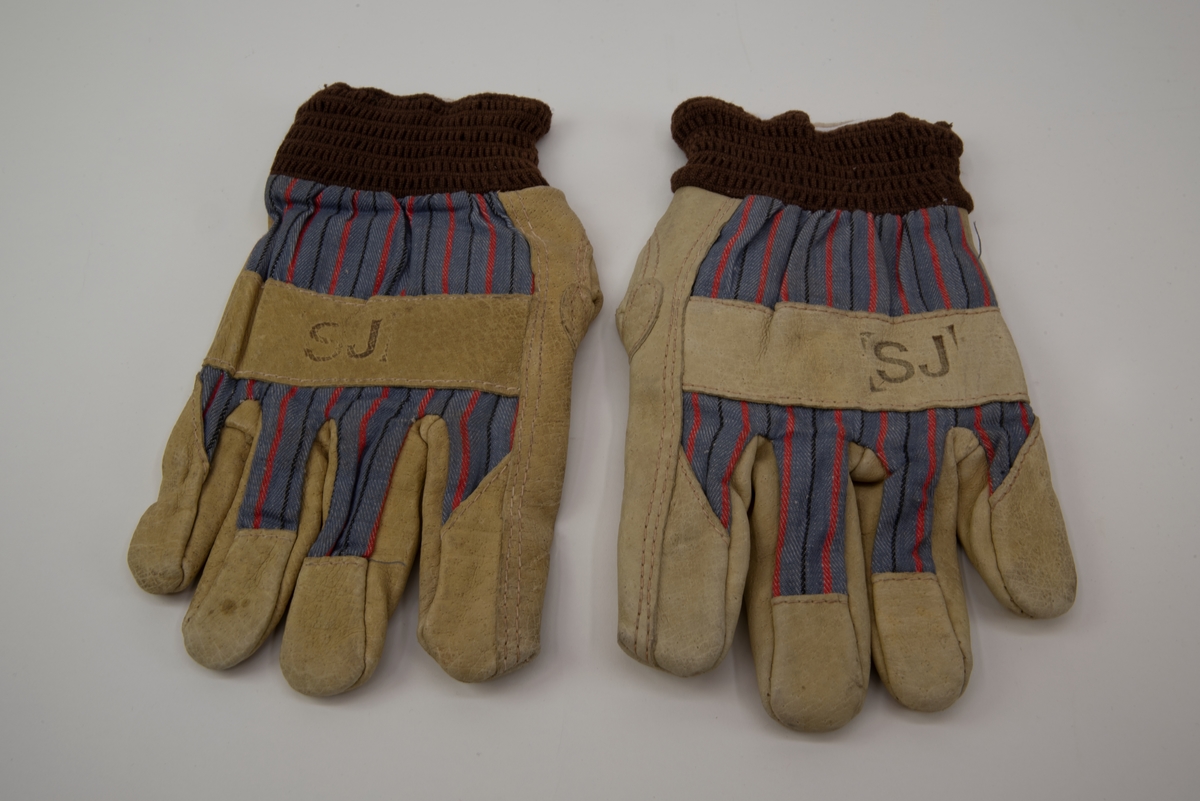 Handskar av ljust skinn och blå, röd, svart randigt tyg med brun resår i öppningarna. Handskarna är fodrade med vitt flanelltyg och har SJ tryckt på utsidan ovanför fingrarna.