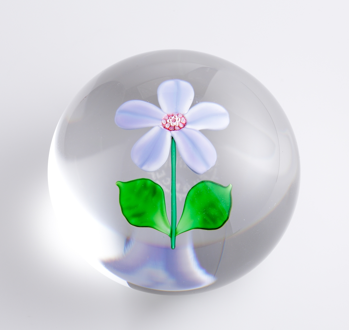 Brevpress, "Floralies Marquerite", med rund form och planad botten. Klarglas med en innesluten lila blomma med grön stjälk och blad. Tillhörande ask med marmorerat mönster.