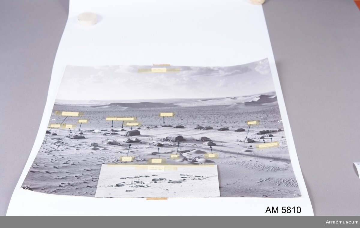 Mått: 700 x 600 mm inkl 50 mm bred ram. Flygfoto över pos 550, Camp Sinai, Egypten. Lappar, fastsatta med tape över foto, visar de olika tältens funktioner. Glaset är sprucket och delvis borttaget upptill.

Samhörande gåva: 5676-5699 + 5800-5827.