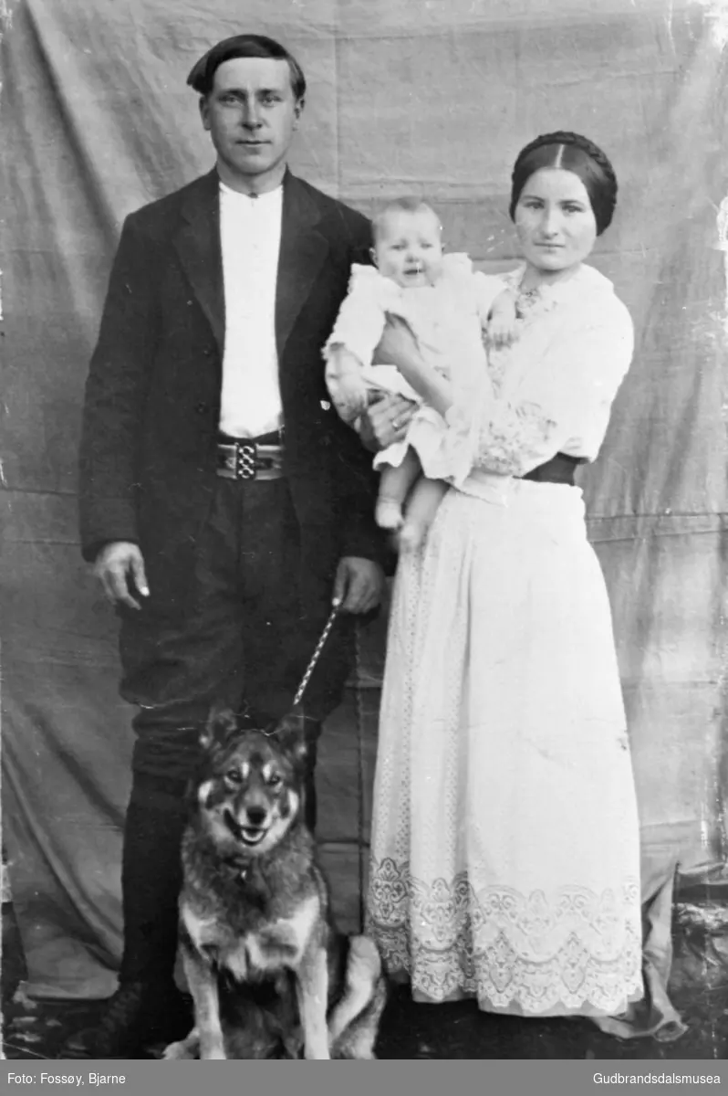 Portrett, familien Dahl; mann og kvinne med lite barn på armen, hund sitter ved deres føtter. 