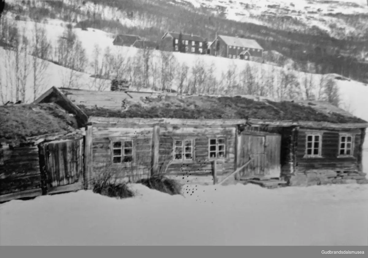Bygning i forgrunnen, gårdsplass litt til høyre i bildet, stugu i Øvre Kvean, fjell i bakgrunnen, det er vinter. 