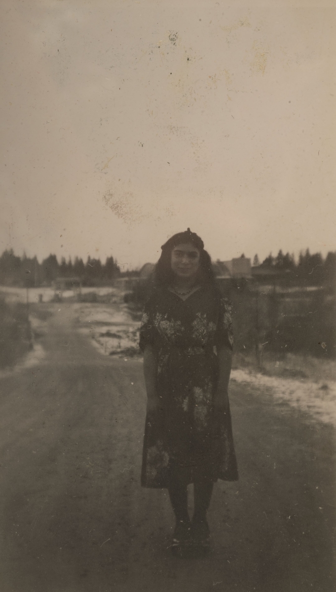 Romsk flicka står på en landsväg i Storvik vintern 1947. I bakgrunden syns idrottsanläggningen Parkhallen som ligger i norra delen av Storvik.