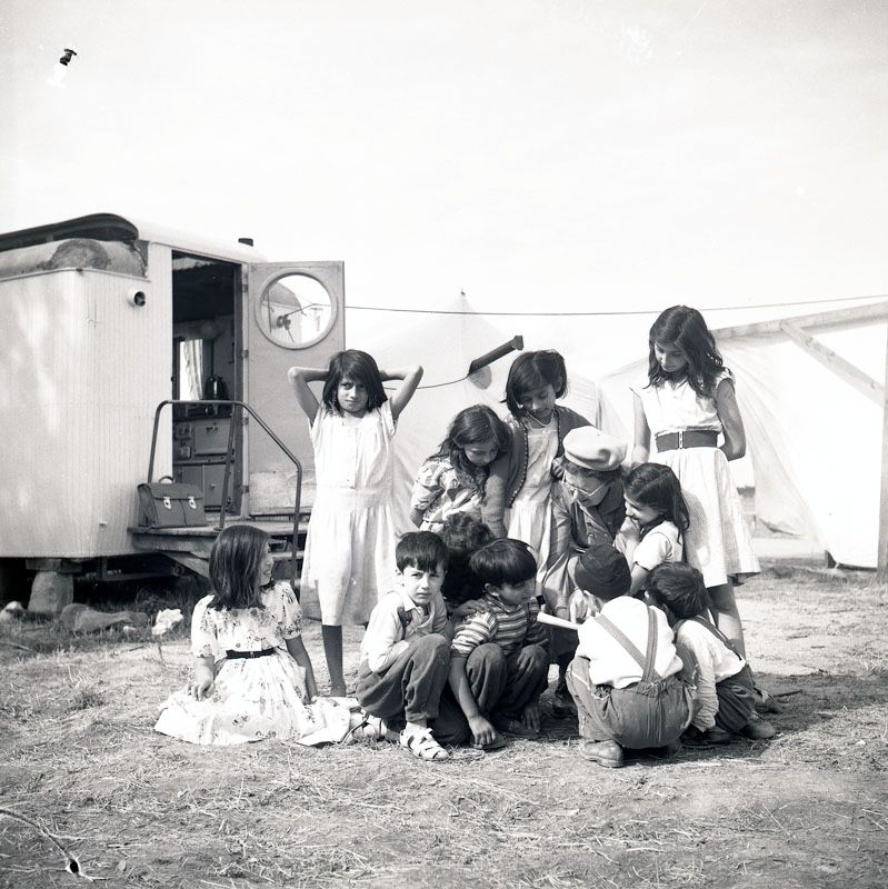 Fotografiet är taget i juli 1952 i samband med skolundervisning i det romska lägret i Ekeby, ca 4 km väster om Eskilstuna. En kvinna, troligtvis lärarinnan, sitter på huk och pekar på ett papper. Runt omkring henne finns 11 barn i olika åldrar, några tittar på pappret och några på fotografen.