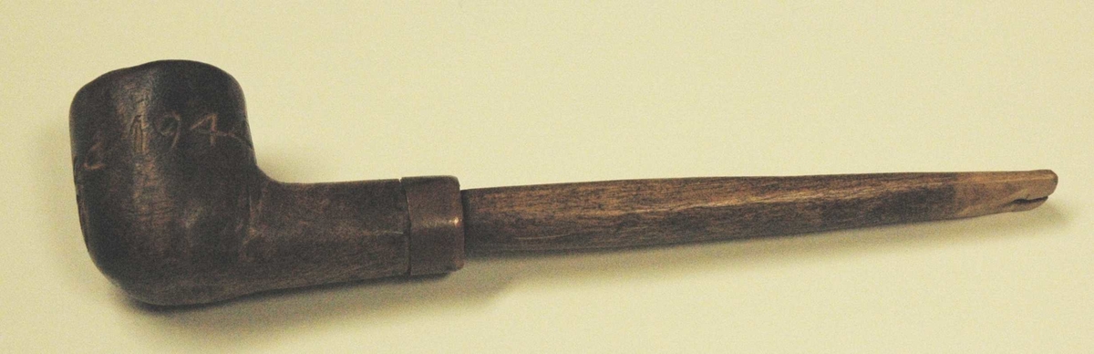 Trepipe med ring (metall) i overgangen mellom pipe og munnstykke. Munnstykket sitter litt løst. I selve pipa er det en inskripsjon.