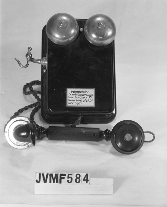 Väggtelefon av svart plåt och bakelit.