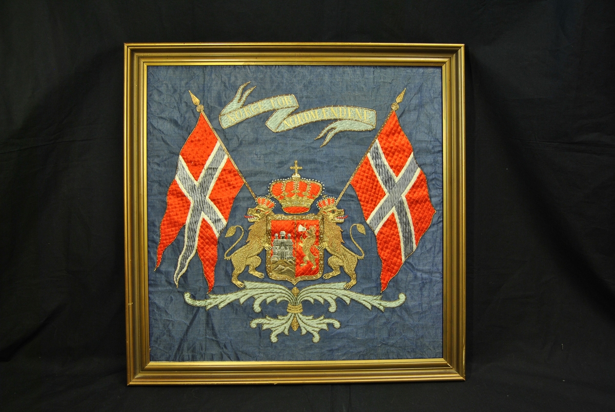I midten er et skjold med løven fra Norges riksvåpen kompinert med Bergens kommunevåpen. På hver side står to løver på bakbeina med krone på. Krone også over skjoldet i midten. Et Norsk flagg på hver side. Banner med ordene Norge for Nordmændene på. Flora nederst.