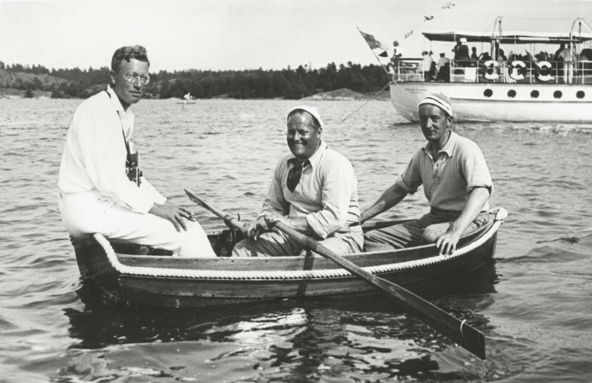 Tre män i en båt under KSSS:s långfärdssegling genom Södermanlands och Östergötlands skärgårdar i juli 1932. I mitten Gunnar Rooth, i aktern David Öhman, i fören oidentifierad person; i bakgrunden Erik Åkerlunds motoryacht STELLA MARINA.
