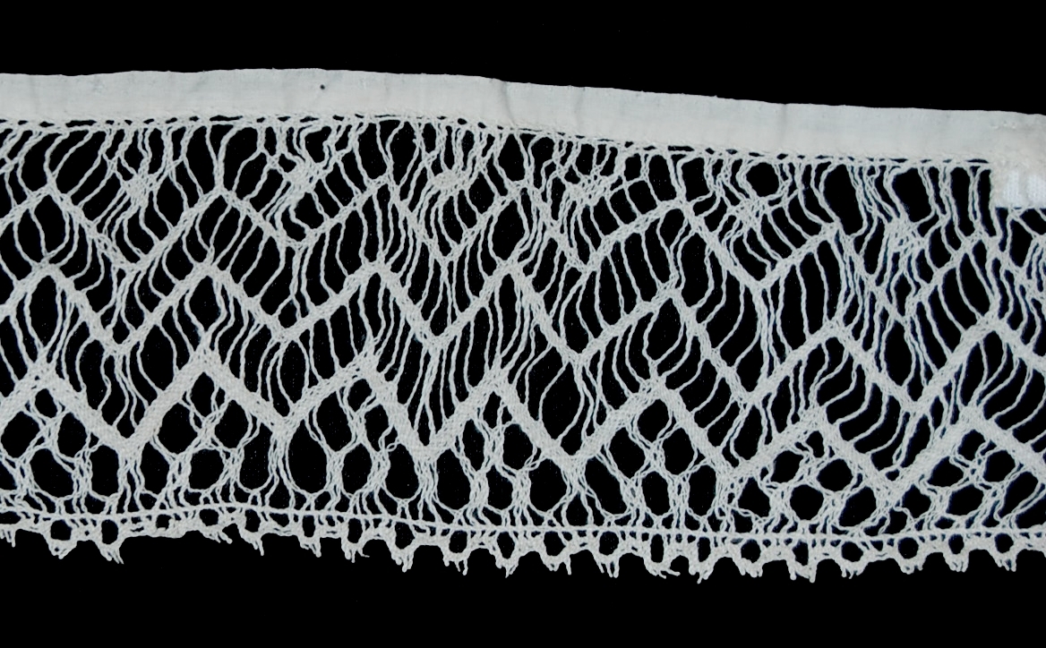 Br: Rättvik-Boda, Dalarna. 
Stycke av spets, dalknyppling, vit lintråd, sydd mot vit bomullslärft. 
Bil. 1 brev