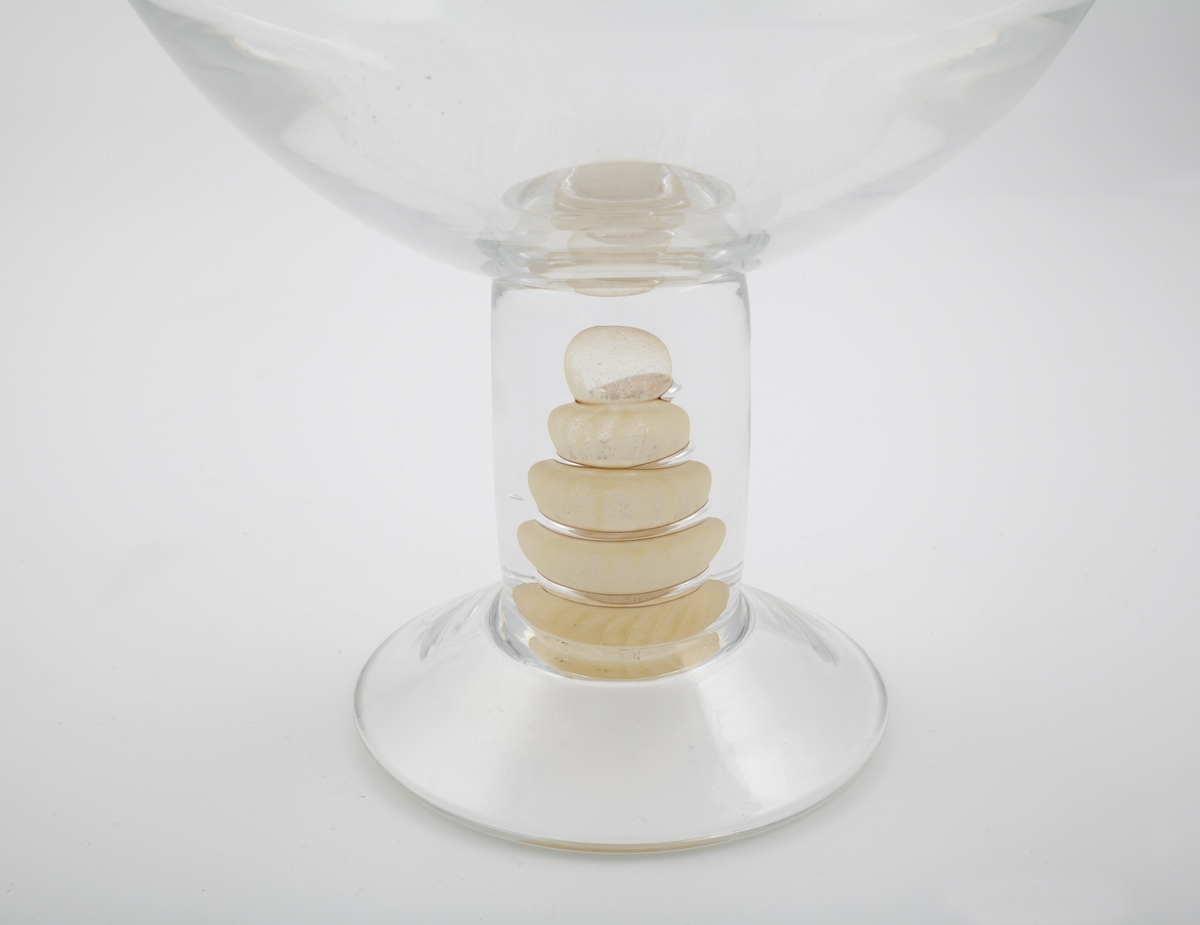 Vase i klart glass. Vid konisk kupa, som bæres av en massiv sirkulær stett. Stetten er dekorert med en spiral i halvgjennomskinnelig sandfarget glass, og hviler på en hevet fotplate.