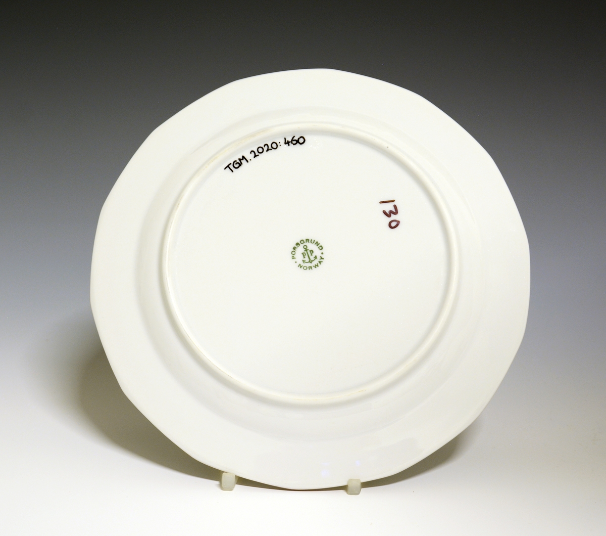 Mangekantet tallerken av porselen med hvit glasur. Dekorert med rød strek ytterst på fanen. 
Modell: Octavia, tegnet av Grete Rønning i 1977.
Dekor: Rød Strek