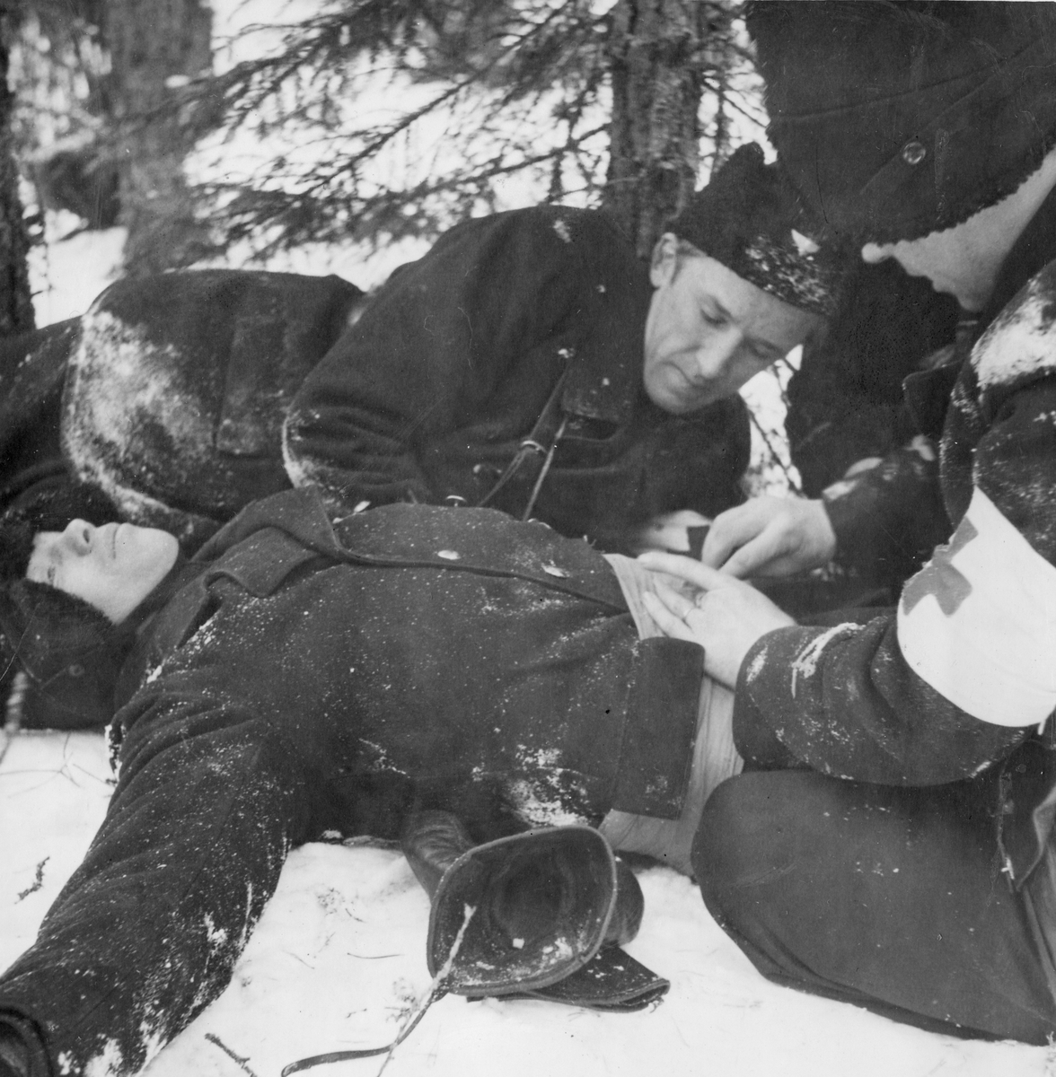 Första hjälpen utförs på soldat som agerar skadad vid sjukvårdsövning i fält vid F 11 Södermanlands flygflottilj, 1945. Omplåstring av skottskada i magen.

Vintertid.

Ur fotoalbum "Sjukvårdsskolan 15/1-15/3 1945" från F 11.