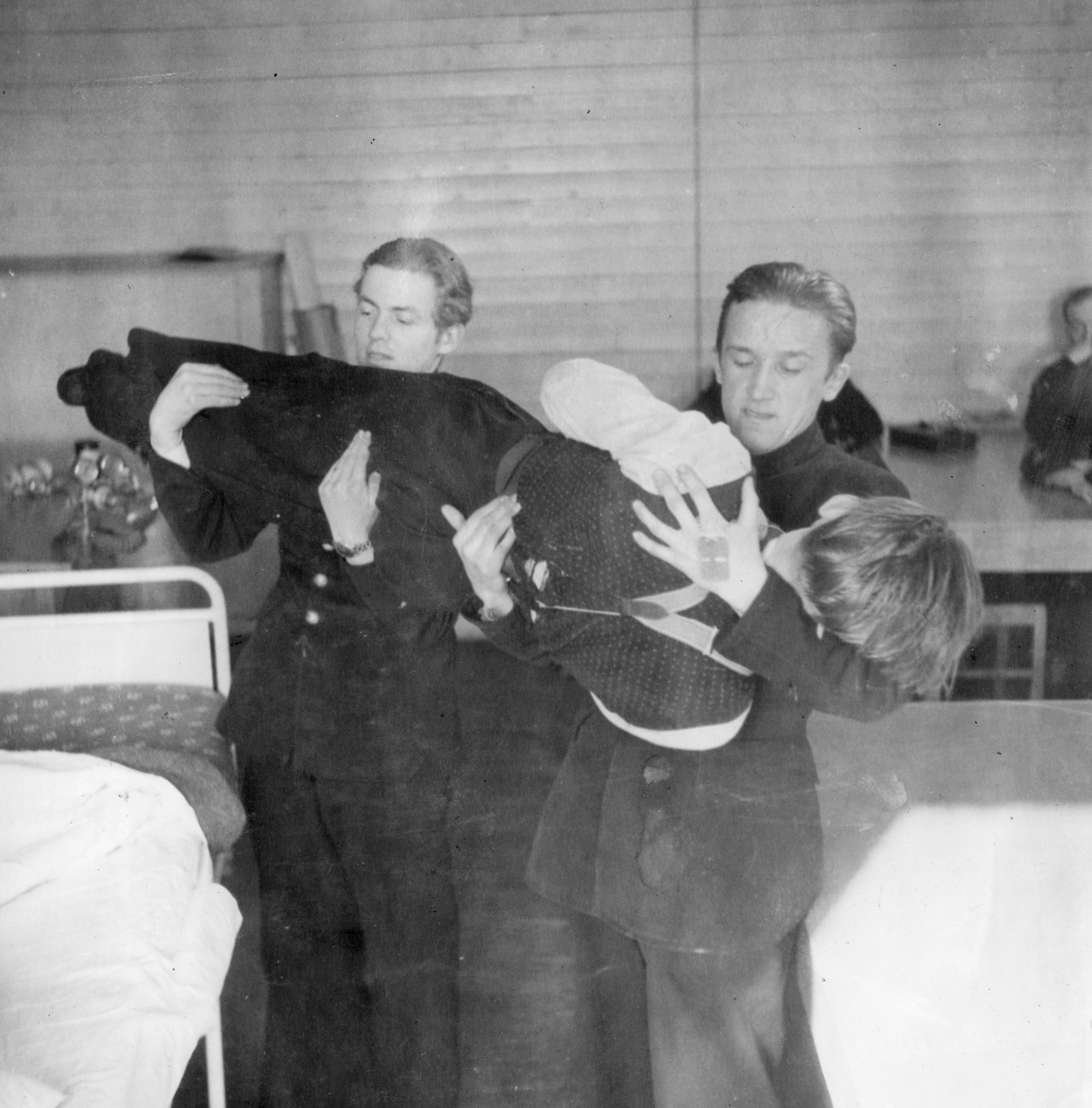 Övning av lyft av skadad vid sjukvårdskurs på F 11 Södermanlands flygflottilj, 1945. Två soldater lyfter en man från en räddningsbår till sjuksäng i skolsal.

Ur fotoalbum "Sjukvårdsskolan 15/1-15/3 1945" från F 11.