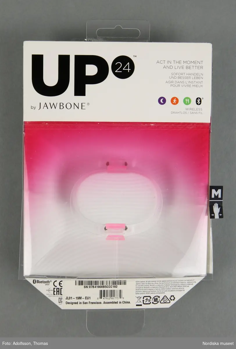 a-b)
Förpackning till Aktivitetsarmband UP24 av märket Jawbone. Består av två delar. a) Den inre delen är formad av vit papp, med fack för USB-kabel, instruktionsbok och aktivitetsarmband. Med fästen av rosatonad plast för armbandet samt skyddsplast för USB-kabel. b) Den yttre delen består av vitt och ceriserosatonat papper samt plast, med varumärke och produktuppgifter på fram och baksida. Förpackningen visar att armbandet är av storlek M (medium). En öppning i ett yttre plastskikt gör det möjligt att kontrollmäta handledens omkrets.