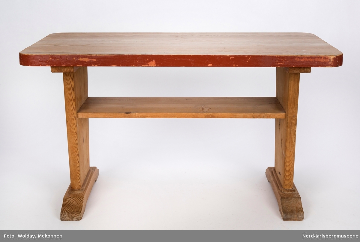 Stuebord med to ben, festet på kortsidene. Tverrgående fotstøtter til bena, bred plate under bordplaten som både stabiliserer og benyttes som hylle. Bordet har en rødtone.