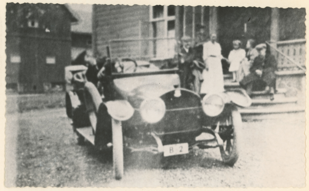Bilen B2 var fra bilenes og drosjenes barndom, ca 1915. I bilen sees eieren Paul Kjellerød. På trappen på Kambo gård: Fra venstre Ludvig Krogsvold, fru godseier Wankel med datteren Elisabeth.
Til høyre Ingar Wankel. Bilen var en tysk Brennabor.