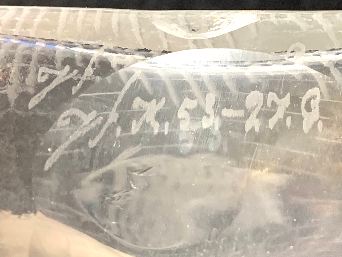 Fyrkantig brännvinsflaska med graverad dekor i form av en metande man på en sjö. I vattnet syns fiskar.
Etikett: Brun botten med svart text "J G"