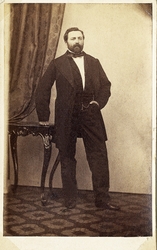 Foto av en skäggig man, klädd i mörk bonjour med väst, stärk