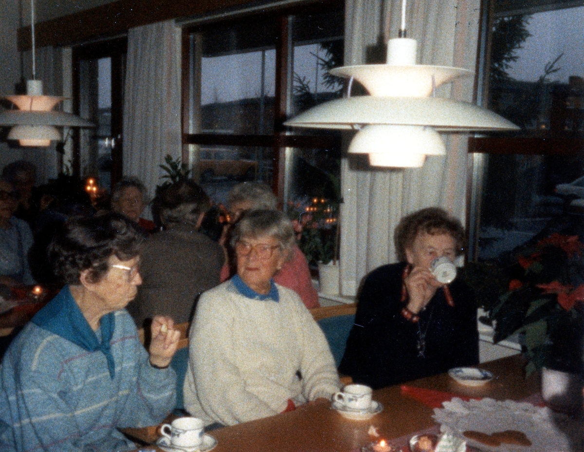 Fikastund i Brattåsgårdens matsal (Streteredsvägen 5), 1980-tal. Från vänster sitter Alma Persson (1910 - 1987), Edit Bernhardsson (1911 - 2000) och Maria Brattberg (1904 - 2000). I taket hänger en vit PH-lampa, formgiven 1924 av den danske arkitekten Poul Henningsen.